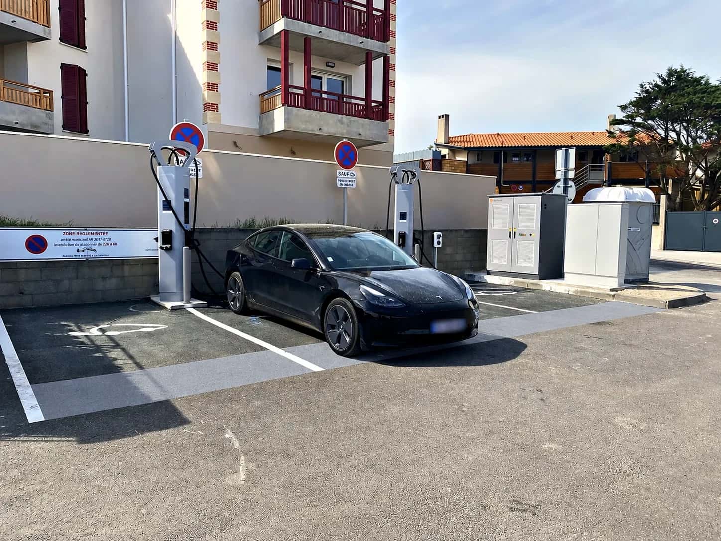 Schwarzes Elektroauto lädt vor zwei Ladestationen am Fuß eines Gebäudes.