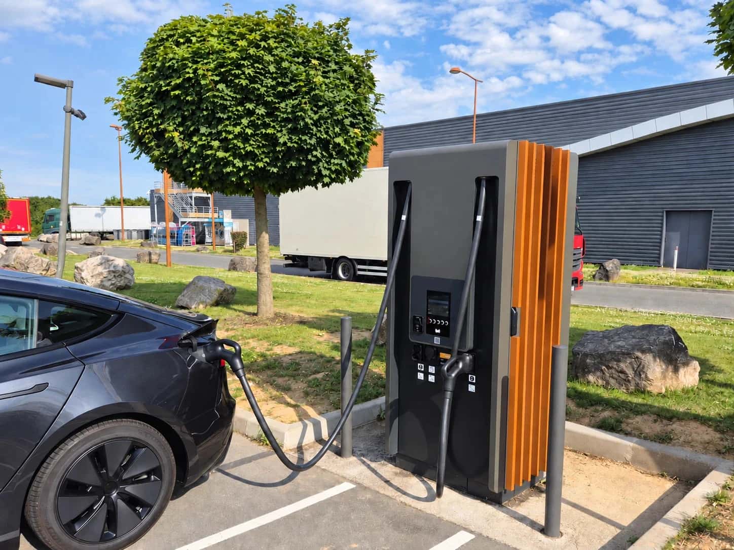 Grauer Tesla an einer holzverkleideten Schnellladesäule