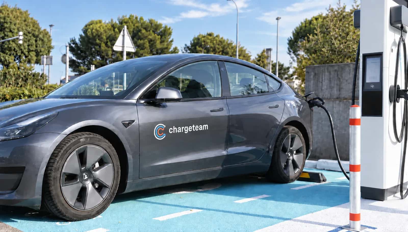 Auto elettrica grigia con il marchio ChargeTeam, in ricarica a una colonnina rapida.