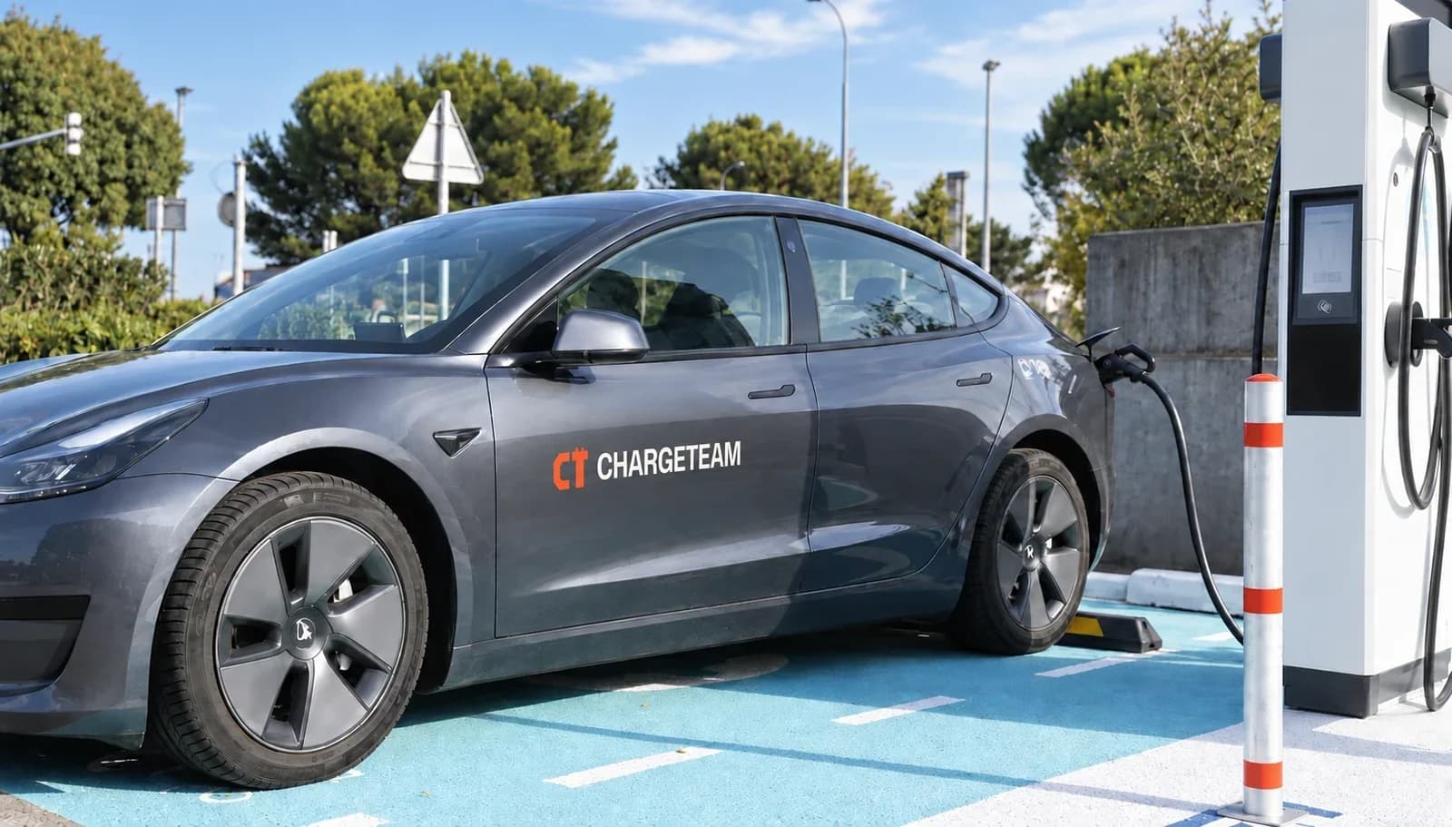 Voiture électrique grise marquée ChargeTeam, en charge sur une borne rapide.