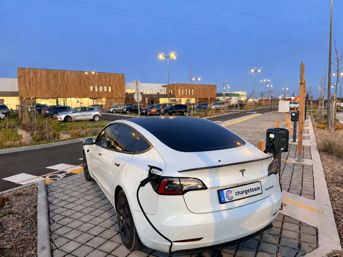 Tesla bianca ChargeTeam collegata a una colonnina, al crepuscolo in un parcheggio aziendale.
