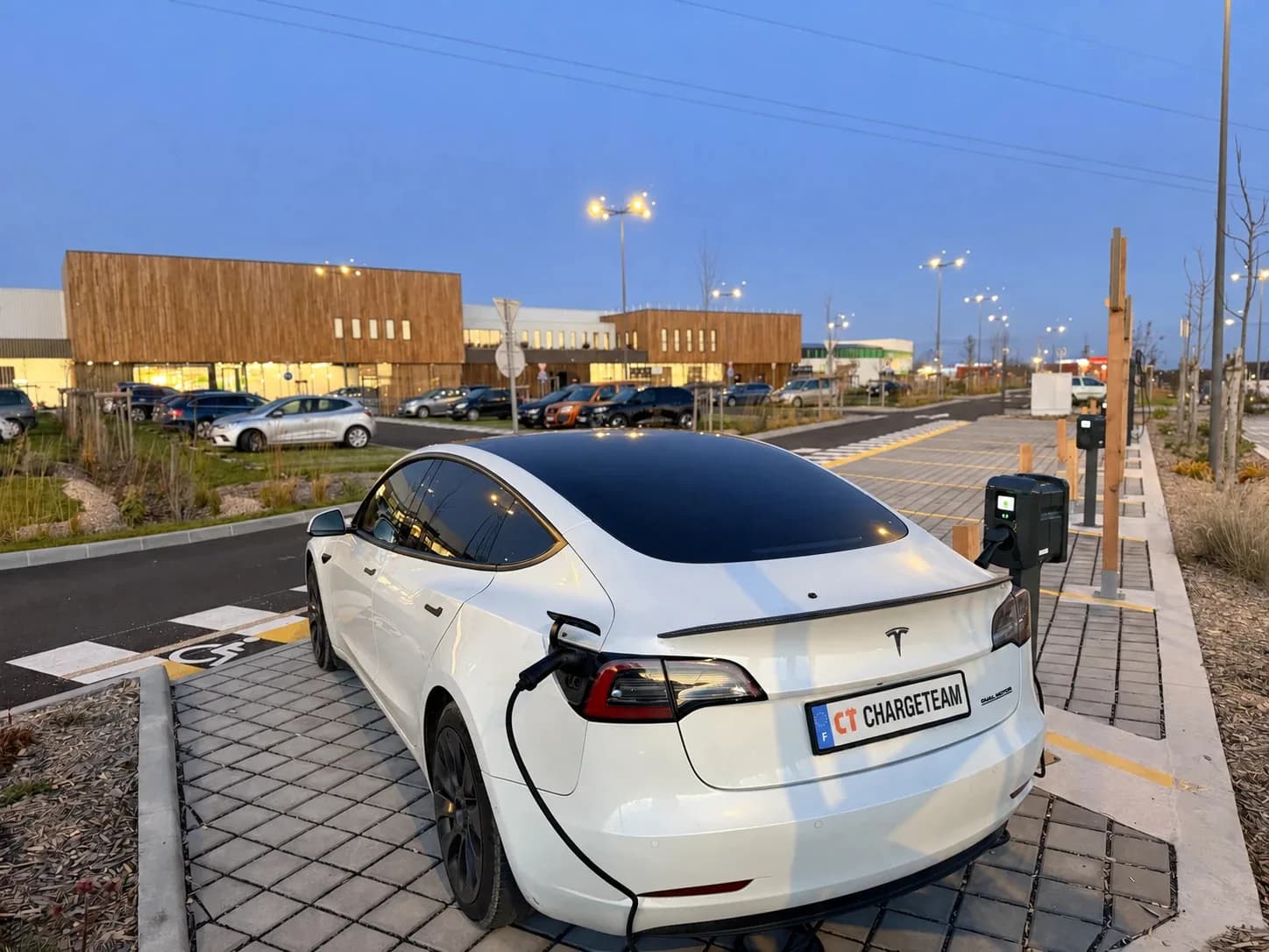 Tesla blanche ChargeTeam branchée à une borne, au crépuscule sur un parking d’entreprise.